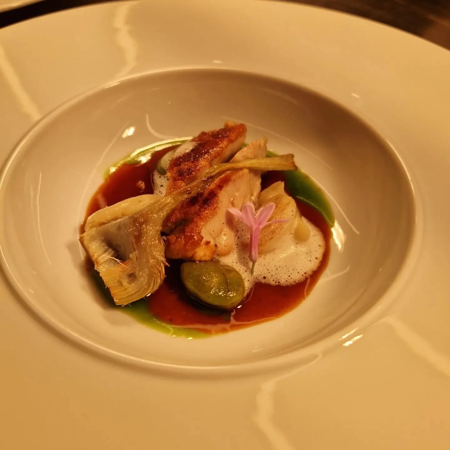 Un plat dressé avec sauce, pickles et une fleur comestible
